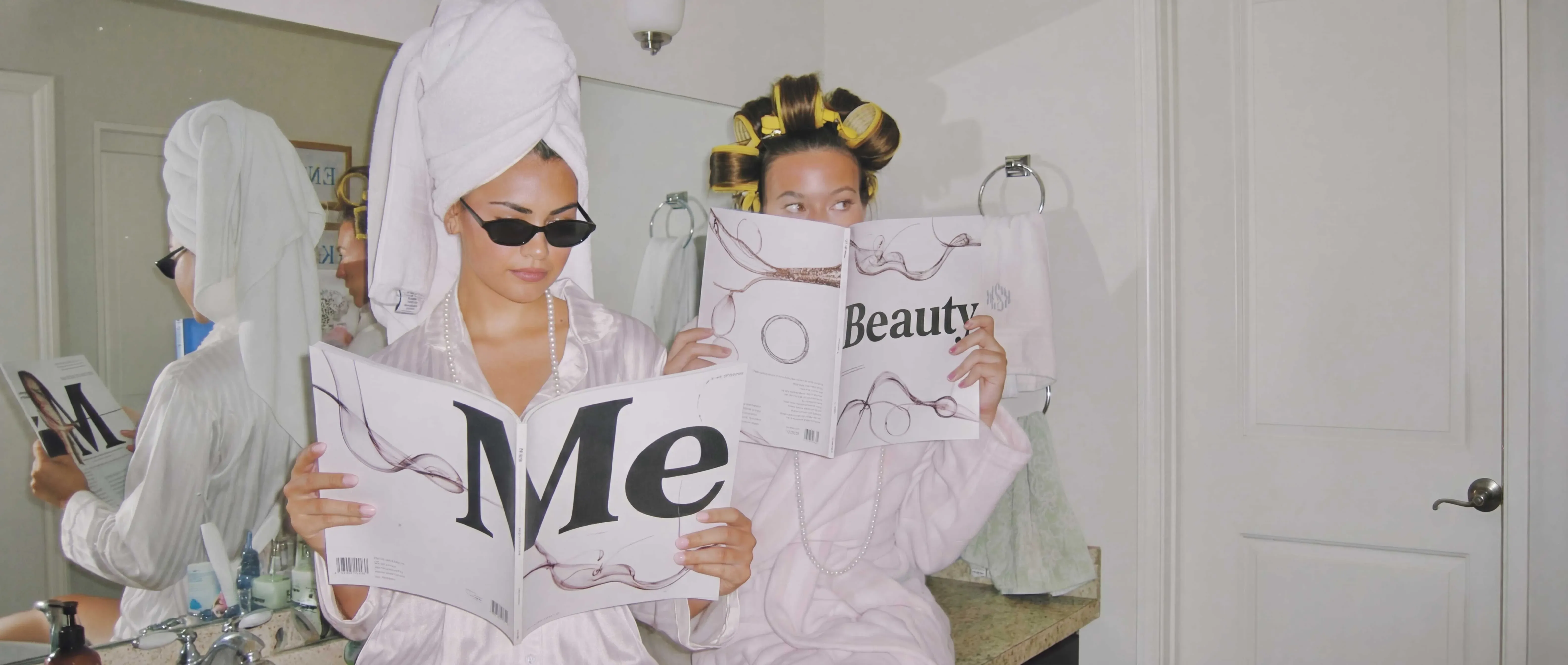 Deux femmes en peignoir lisant un magazine Me&Beauty dans une salle de bain, illustrant l’univers et l’histoire de la marqu