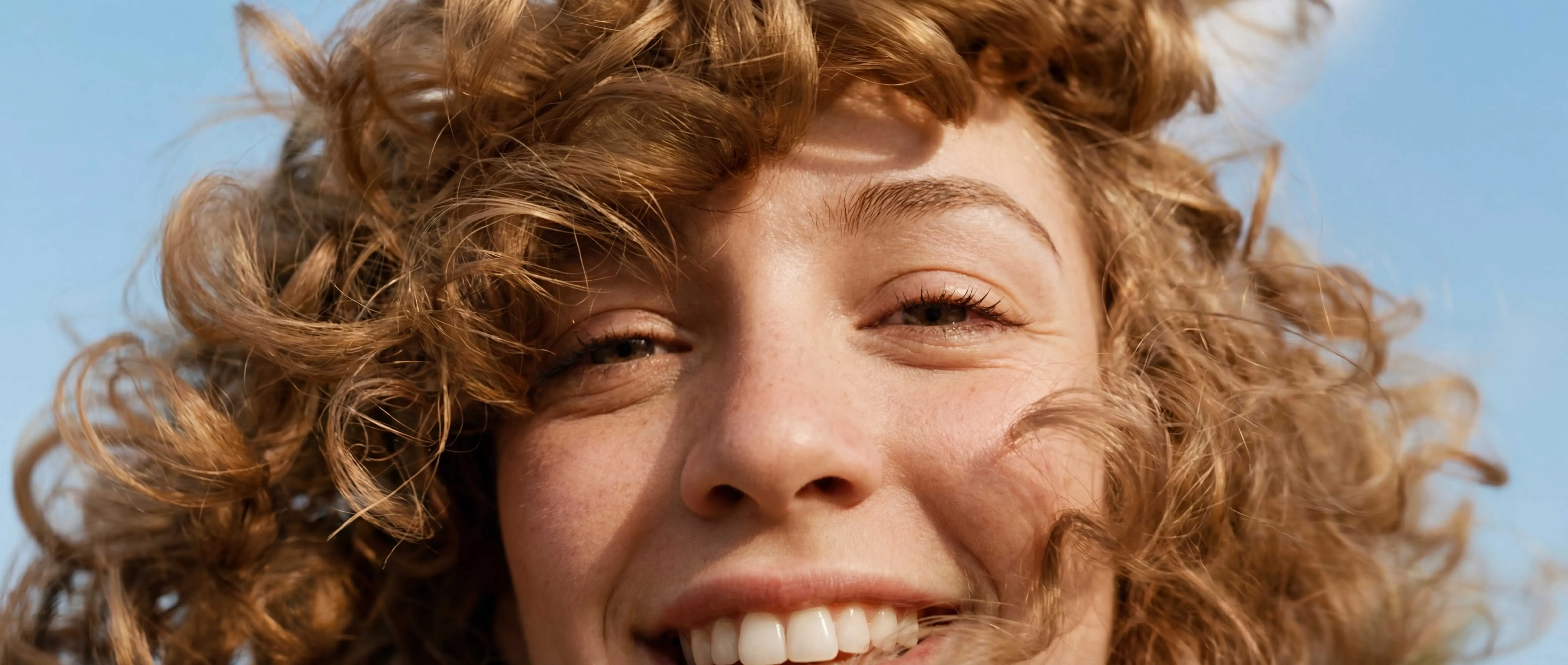 Gros plan d’un visage souriant avec des cheveux bouclés au soleil.”